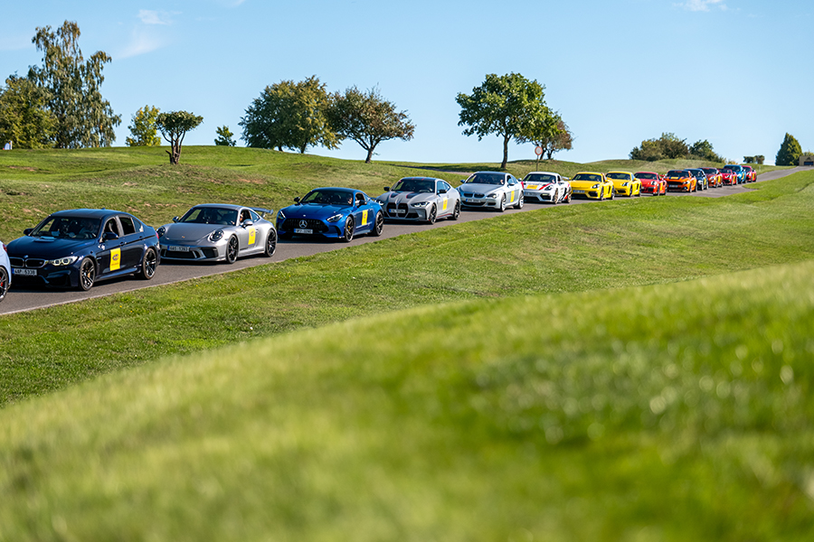Colonna di auto sportive con il logo Magneti Marelli Parts & Services su una strada asfaltata circondata dal verde durante un evento incentive a Praga per i partner italiani.
