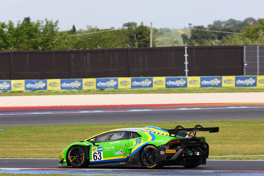Vettura GT in pista con logo Magneti Marelli Checkstar sulla tabella porta-numero e cartellonata a bordo pista sullo sfondo